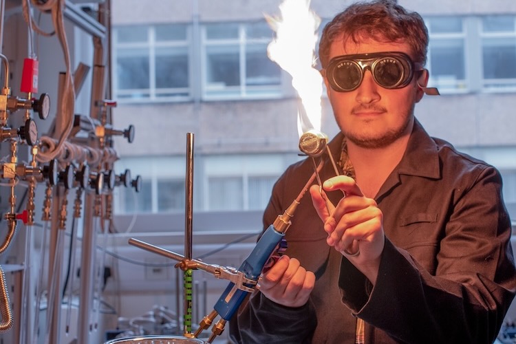 Student wearing safety goggles conducts a flame experiment in a laboratory.